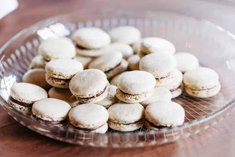 Eine Glasplatte mit einem Stapel heller Macarons mit dunkler Füllung, die auf einer Holzunterlage angeordnet sind.