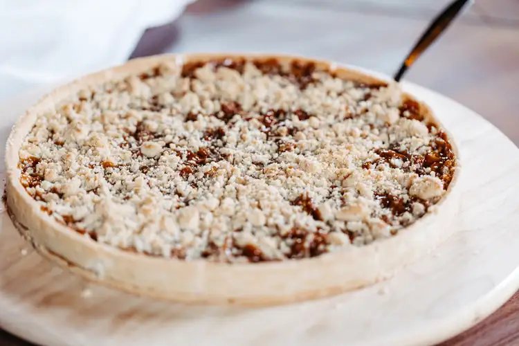 Nahaufnahme eines frisch gebackenen Kuchens mit Streuselauflage, der auf einem runden Marmorbrett platziert ist. Ein Kuchenservierer ist teilweise am Rand des Kuchens sichtbar.