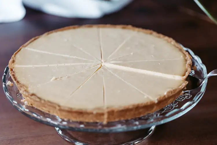 Ein in Scheiben geschnittener Käsekuchen mit goldbrauner Kruste steht auf einem gläsernen Kuchenständer und ist bereit zum Servieren.
