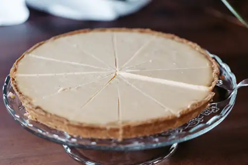Ein in Scheiben geschnittener Käsekuchen mit goldbrauner Kruste steht auf einem gläsernen Kuchenständer und ist bereit zum Servieren.