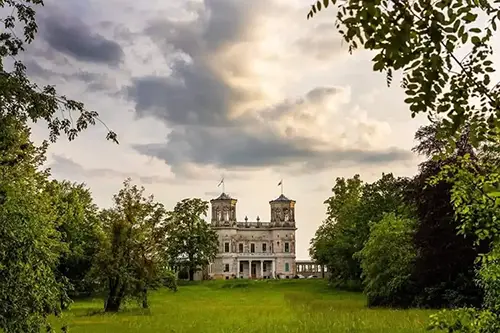 Eingebettet in üppiges Grün bietet das historische Schloss mit seinen ikonischen Türmen eine malerische Kulisse für ein Hochzeits- und Feiererlebnis im Lingnerschloss Dresden. Der dramatische Himmel, aufgenommen von Melanie Kunert Fotografie-Hochzeitsfotografin Dresden, verstärkt seinen zeitlosen Reiz.