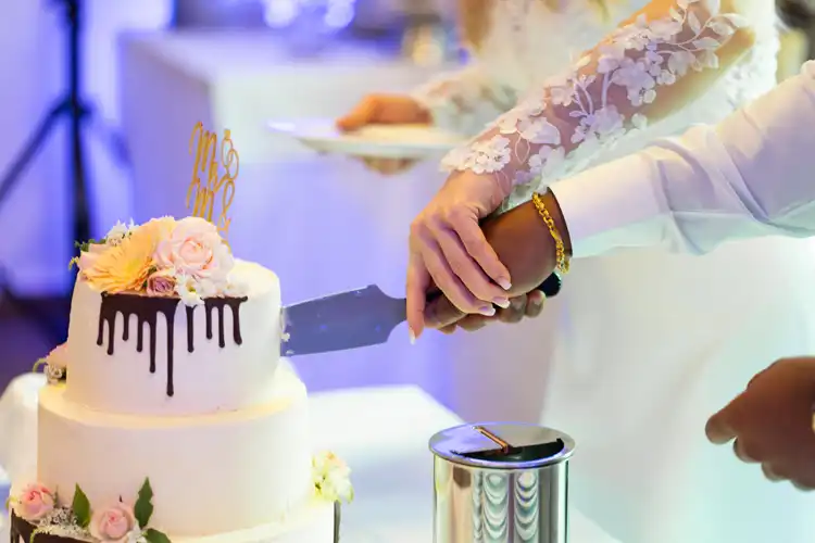 Braut und Bräutigam schneiden auf Hochzeit Gut am See eine weiße, mit Blumen und Schokostreuseln verzierte Hochzeitstorte an. Der Hochzeitsfotograf Görlitz hat diesen Moment wunderschön eingefangen; die Braut trägt ein Kleid mit Spitzenärmeln.