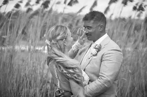 Braut und Bräutigam umarmen sich in einer Wiese mit hohem Gras auf der Hochzeit Gut am See. Das Schwarz-Weiß-Foto von Hochzeitsfotograf Görlitz fängt den Moment der Zuneigung am Hochzeitstag ein.