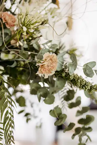 Nahaufnahme eines Blumenarrangements mit blassrosa Nelken, Eukalyptusblättern und zarten weißen Blumen - perfekt für eine Hochzeit auf Gut am See -, das vor einem unscharfen Hintergrund ein weiches, natürliches Aussehen erzeugt.