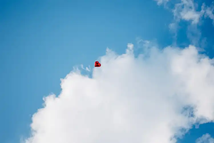 Ein roter herzförmiger Ballon schwebt über einer weißen Wolke vor einem strahlend blauen Himmel - eine bezaubernde Szene, perfekt für eine Hochzeit auf Gut am See, wunderschön eingefangen von einem Hochzeitsfotograf Görlitz.