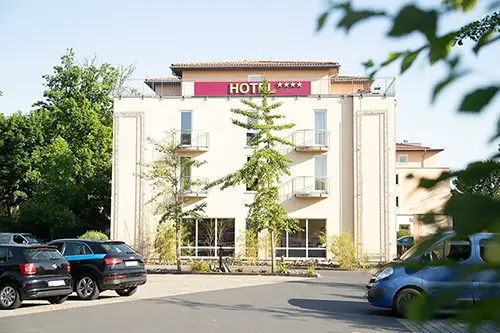 Ein Vier-Sterne-Hotel mit großem Schild, umgeben von Bäumen und Sträuchern, bietet eine zauberhafte Kulisse für eine Hochzeit im Berghotel Wilder Mann. Fahrzeuge parken auf dem sonnendurchfluteten Parkplatz, drinnen wartet die Kunst der Hochzeitsfotografin Dresden-Melanie Kunert Fotografie.