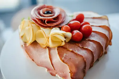 Herzförmige Wurstwaren mit Wurstschichten, Salamirosette, Käseblüten und Kirschtomaten auf einem weißen Teller – perfekt für eine Hochzeit in Tharandt.