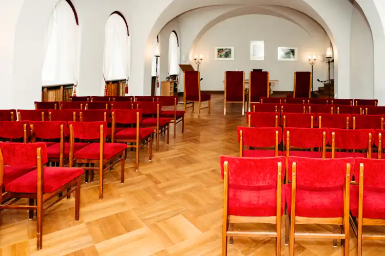 In einem hellen Raum mit Bogenfenstern, Holzfußboden und gerahmten Bildern stehen rote Polsterstühle in Reih und Glied im Standesamt Görlitz - eine elegante Kulisse, die sich perfekt für eine Zeremonie eignet und von Hochzeitsfotograf Görlitz wunderschön eingefangen wurde.