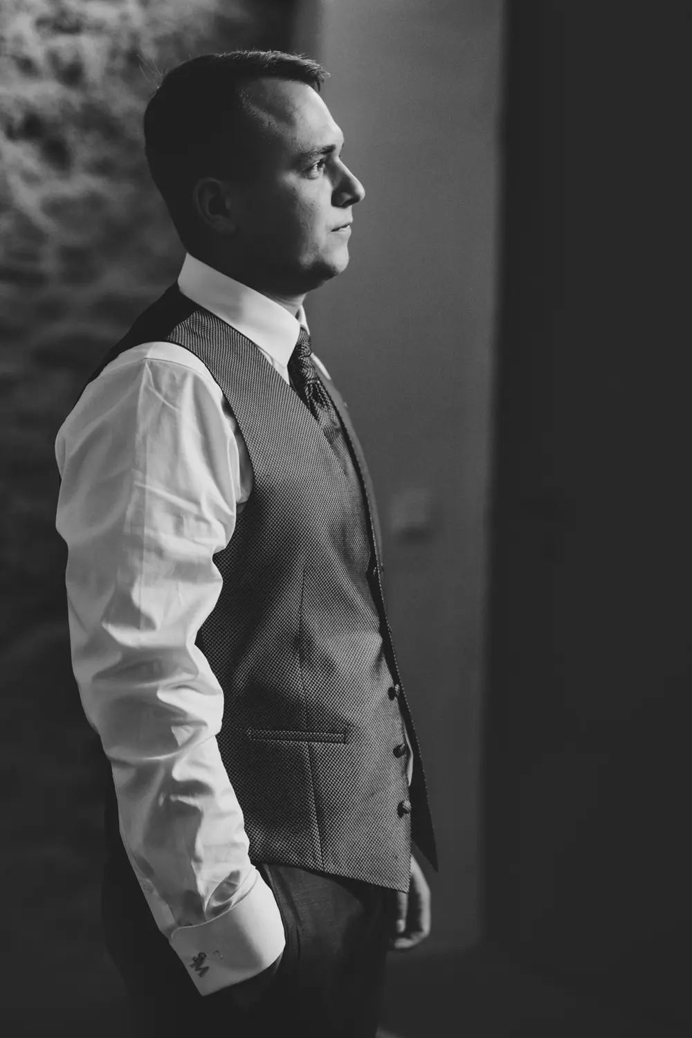 Ein Mann in Hemd, Krawatte und Weste steht im Profil und schaut nachdenklich. Das Bild ist in Schwarz-WeiĂź gehalten, mit einem unscharfen Hintergrund und einer weichen Beleuchtung, die sein Gesicht hervorhebt.