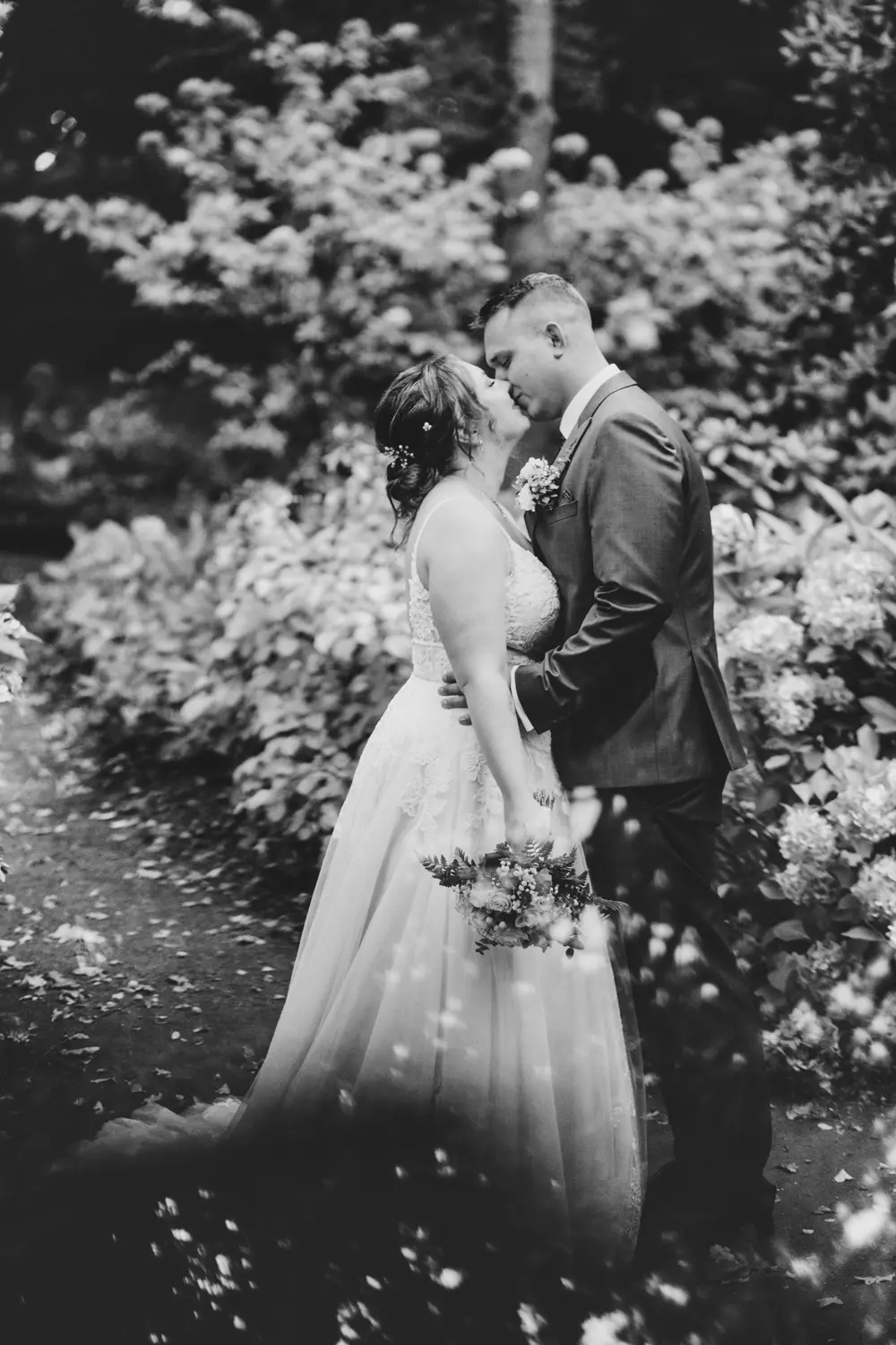 Ein Mann und eine Frau, die sich vor einem GebĂĽsch kĂĽssen.